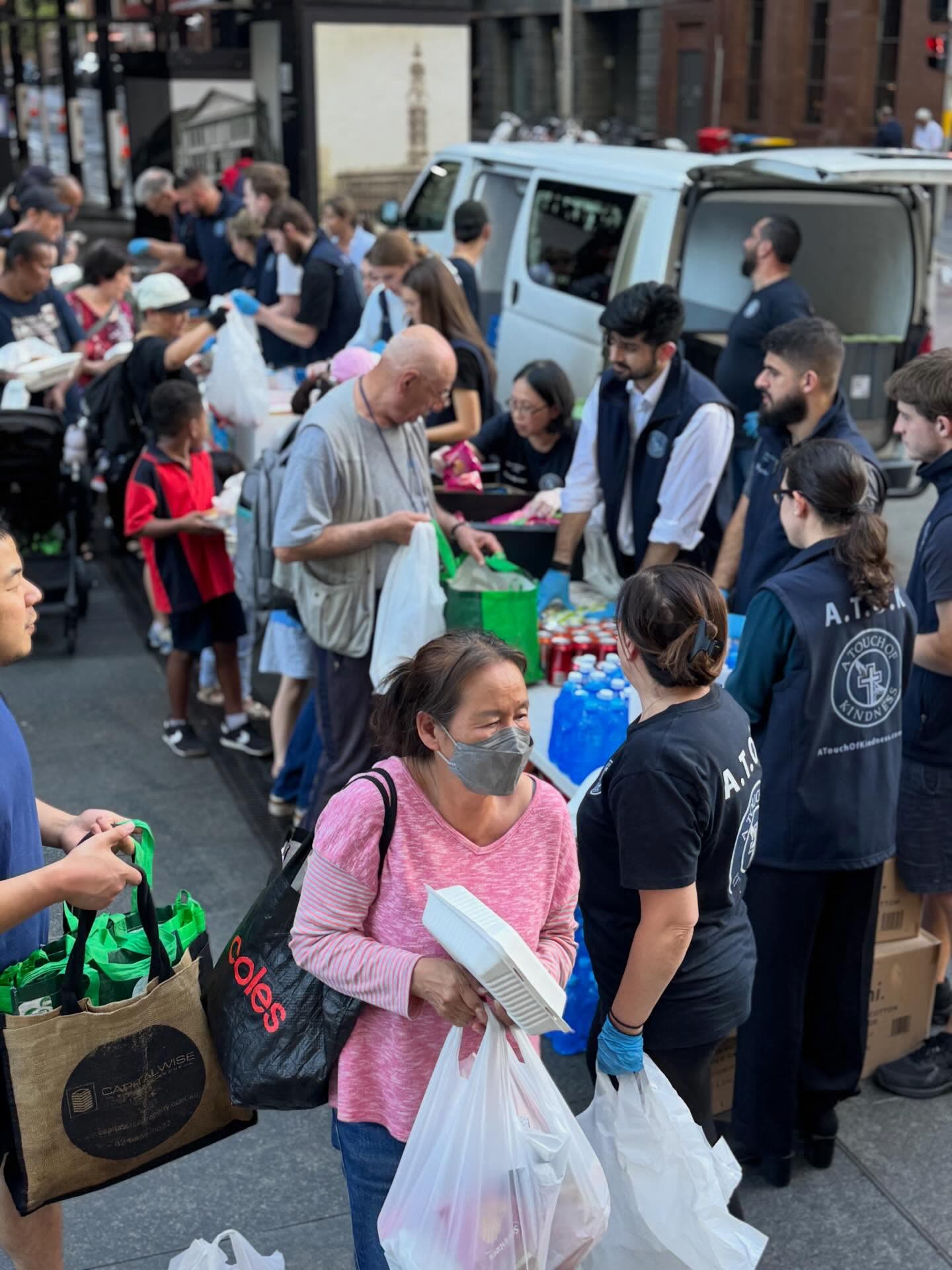 Volunteers handing bags of groceries to people at the back of the van